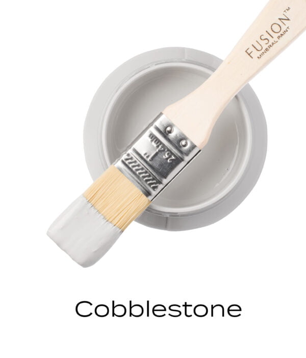 An angled brush that has been dipped in, and then placed on top of an open pint of Cobblestone Fusion mineral paint to indicate the colour.