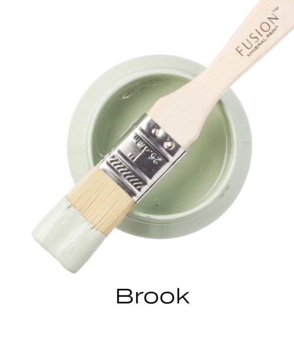 An angled brush that has been dipped in, and then placed on top of an open pint of Brook Fusion mineral paint to indicate the colour.